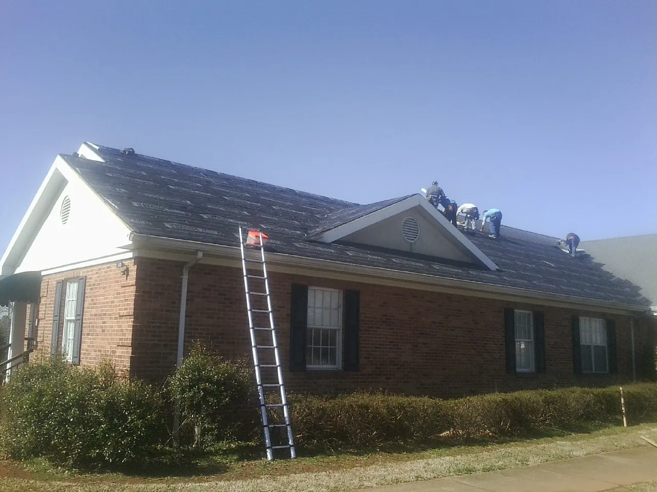 Crew tearing shingles off a brick ranch roof with a ladder set — Emergency Roof Repair work by our crew in Grand Island